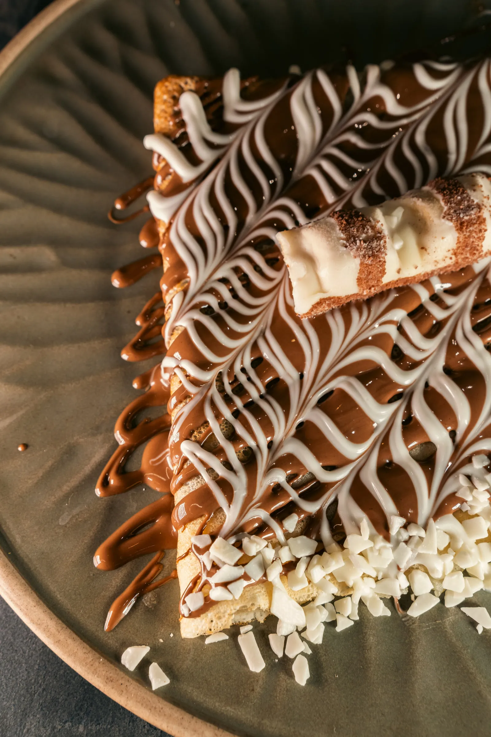 Crêpe folded on a plate, piped with dark and white chocolate in a feather pattern and scattered with almond flakes
