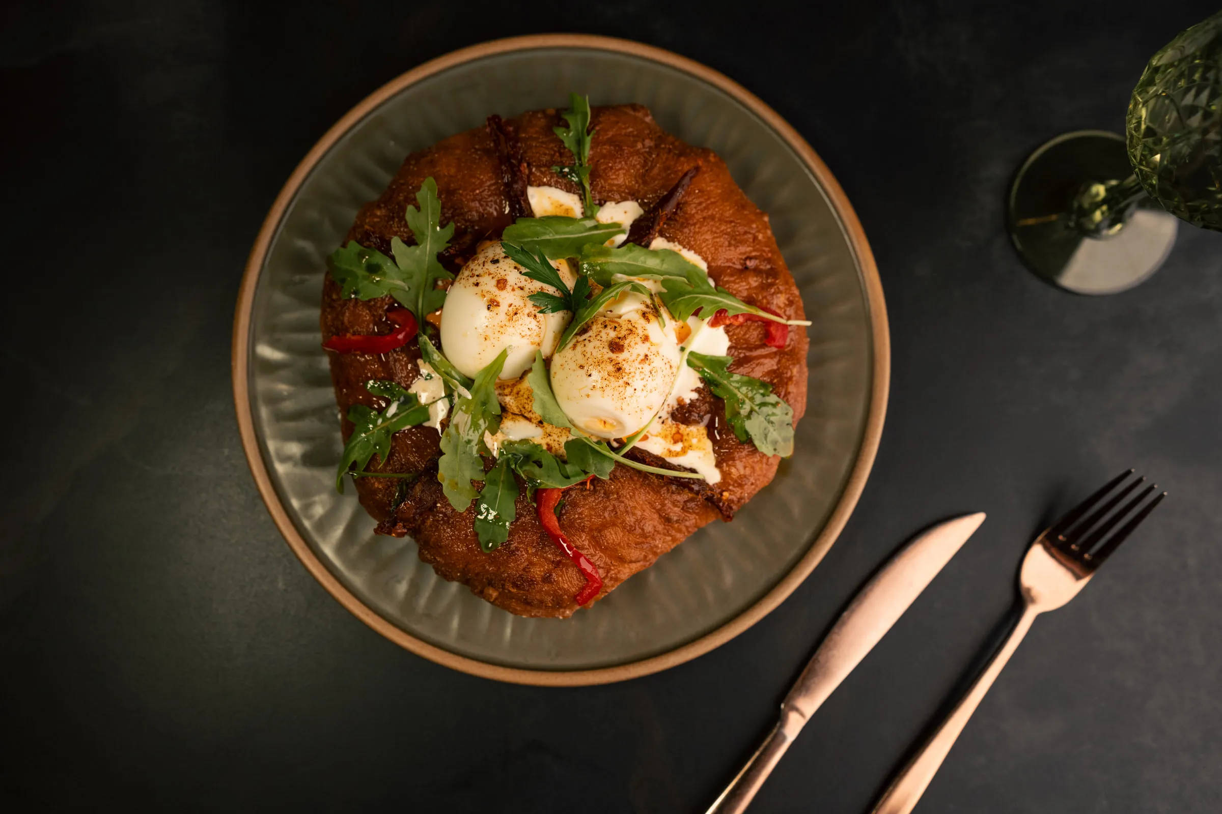 Poached eggs on toasted bread with yoghurt, chilli butter and rocket, rose-gold cutlery beside the plate