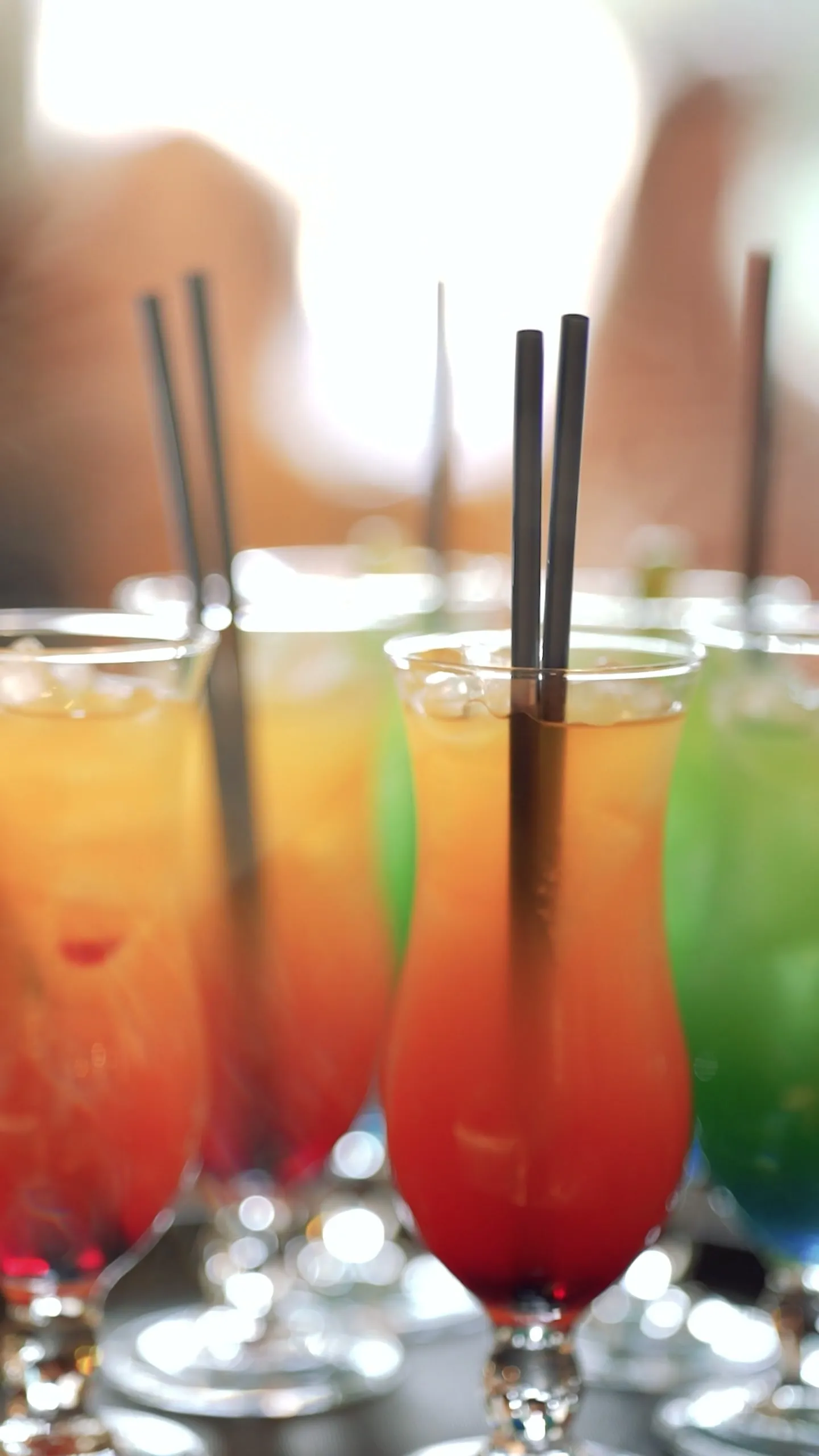 Layered orange, red and green mocktails in tall glasses with black straws