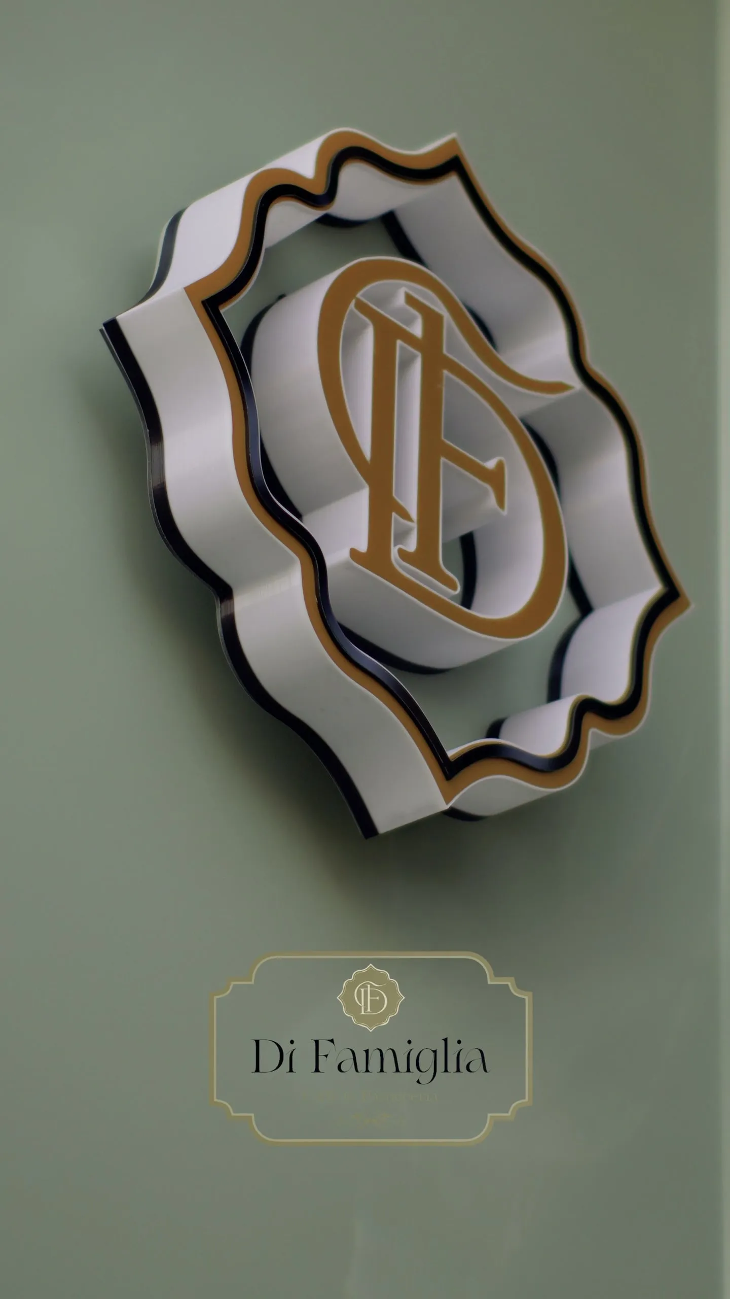 The white and gold Di Famiglia emblem sign mounted on the sage façade