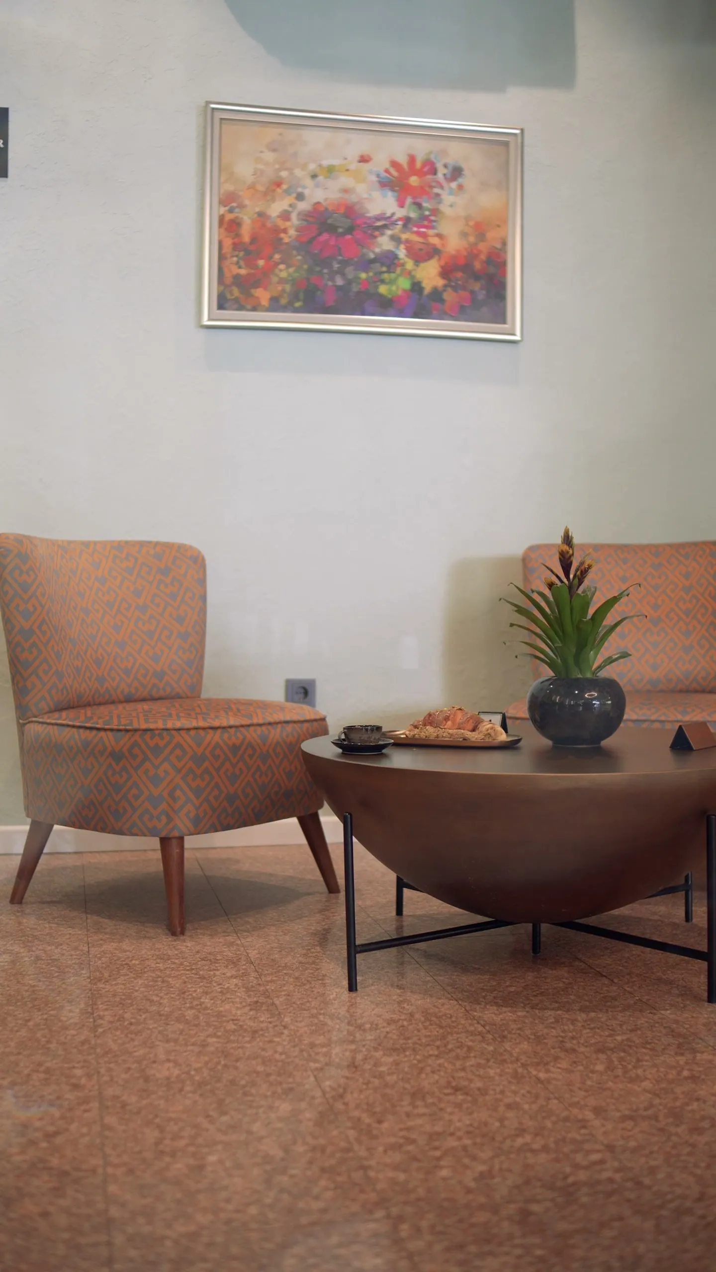 The lounge corner: two armchairs, a round wooden coffee table and a flower painting on the wall