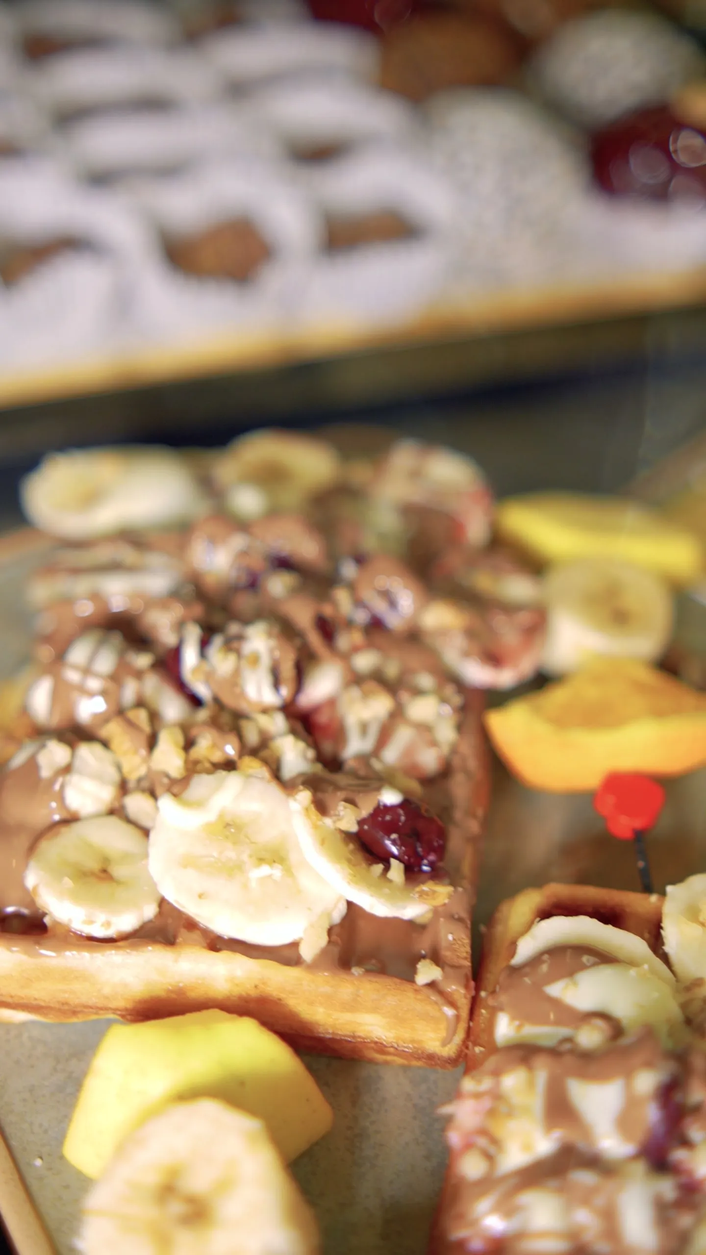 Pastries topped with banana, walnuts and cherry, with coconut sweets behind