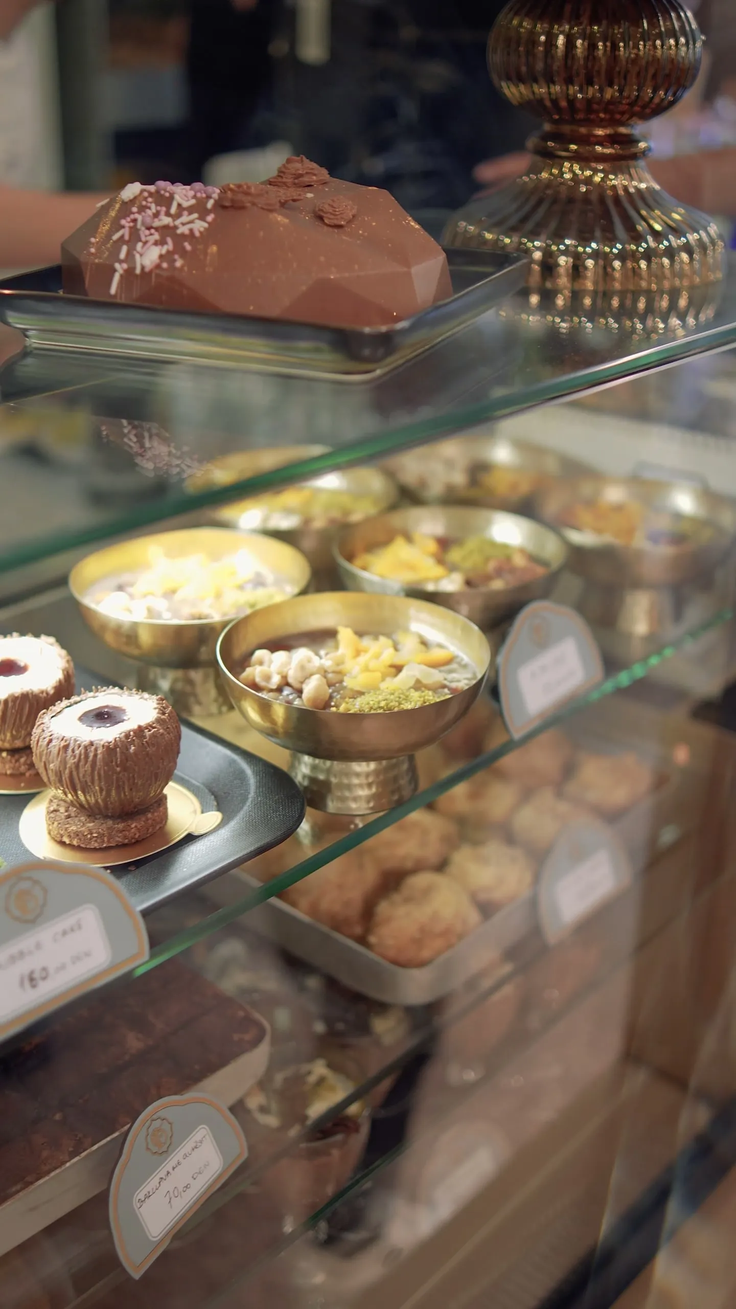 The pastry vitrine: a chocolate cake, gold bowls of desserts and trays of pastries on glass shelves